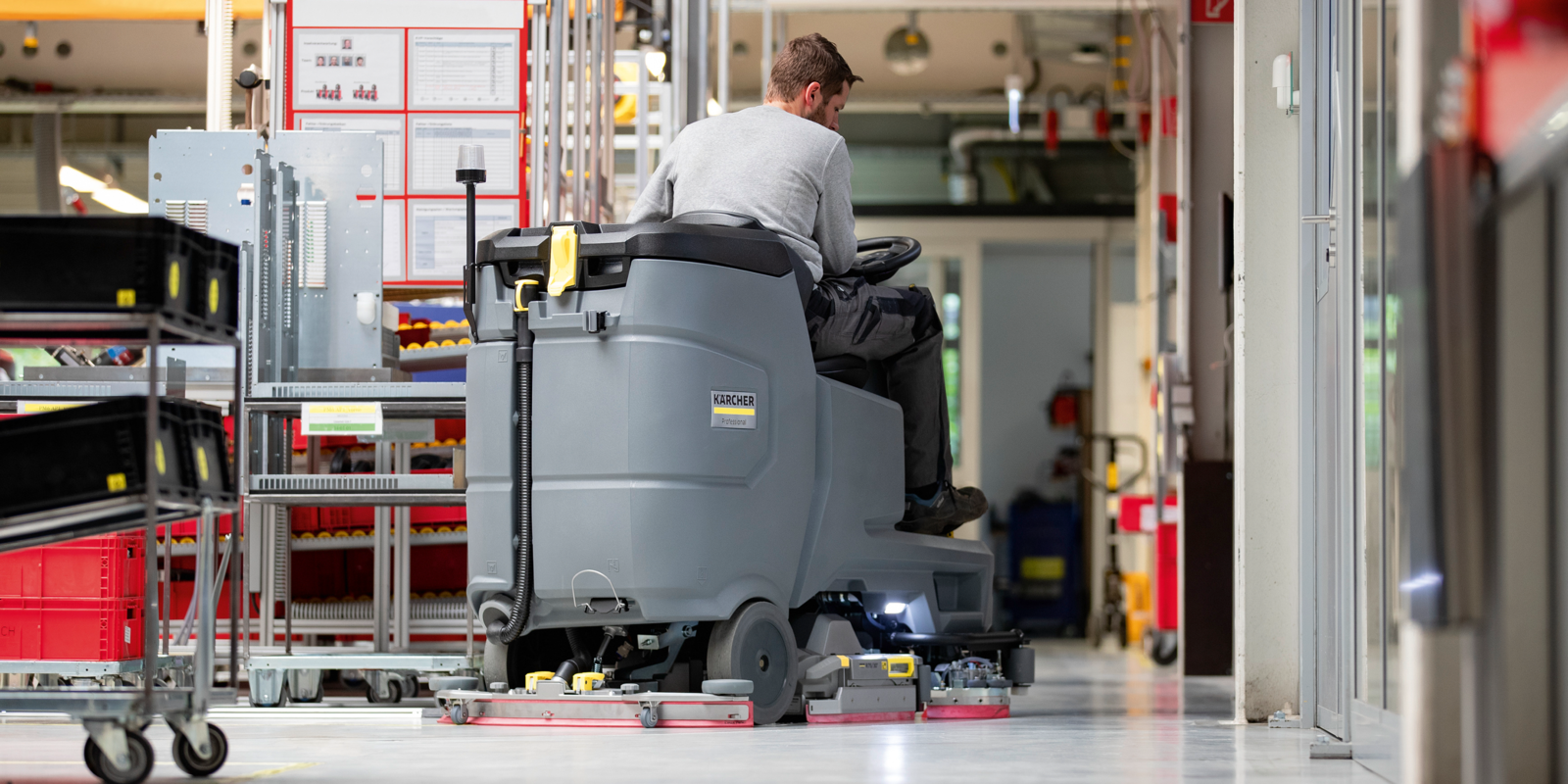Mann sitzt auf Scheuersaugmaschine. Mann sitzt auf Scheuersaugmaschine und kehrt Boden in Logistikhalle.