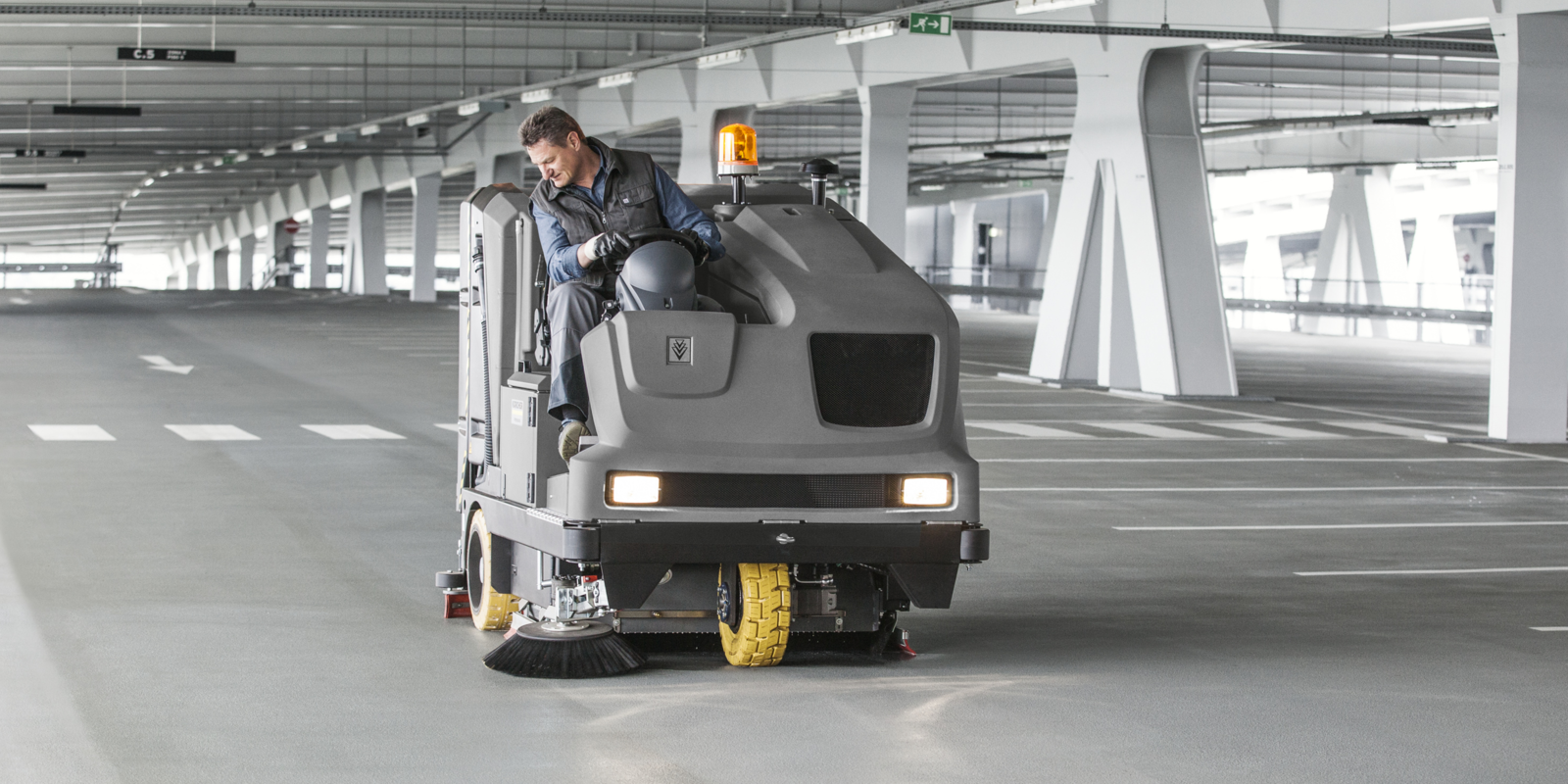Mann sitzt auf Scheuersaugmaschine. Mann sitzt auf Scheuersaugmaschine und kehrt Boden in Parkhaus.