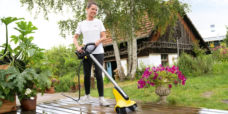 Μια γυναίκα καθαρίζει το ξύλινο δάπεδό της με καθαριστικό αίθριου Kärcher