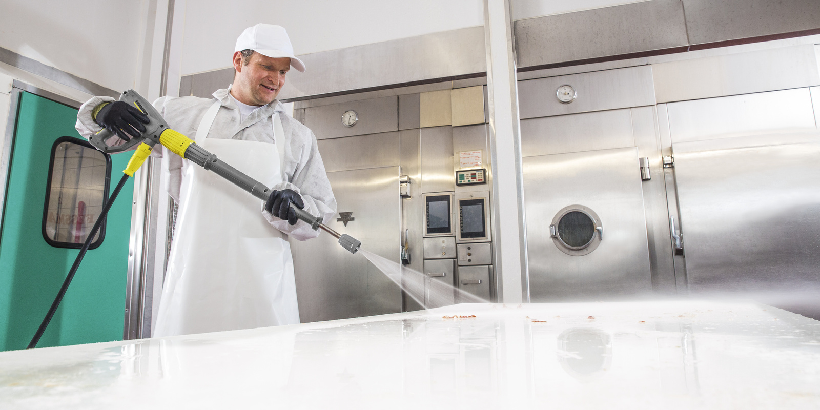 Surface disinfection with high pressure washers for butchers A man in white work clothes cleans a work surface with a Kärcher high-pressure washers