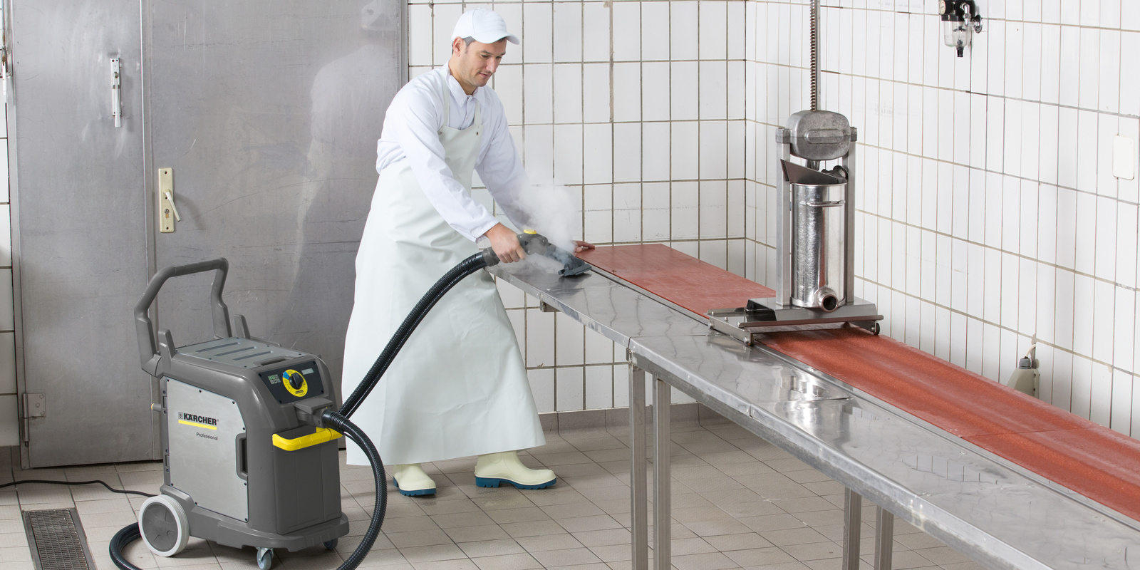 Disinfection using steam for butcher’s shops A man in white work clothes cleans a work surface with a Kärcher steam vacuum cleaner