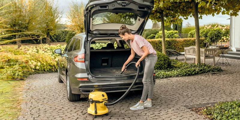 Μια γυναίκα σκουπίζει το πορτμπαγκάζ του αυτοκινήτου με την ηλεκτρική σκούπα Kärcher