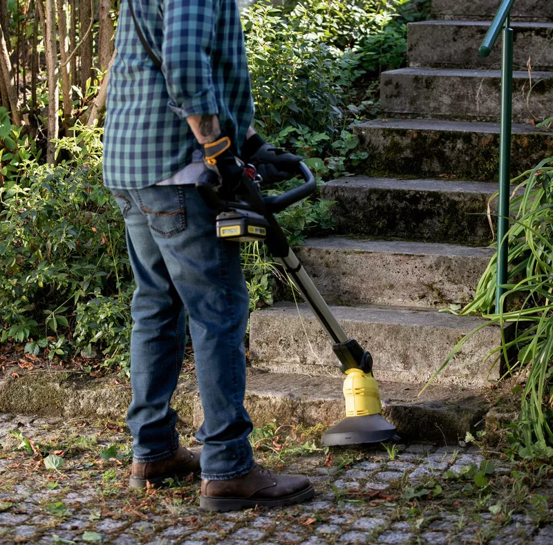 A man wearing ear defenders cleans the paving stone joints in front of a staircase with a Kärcher Weed Remover