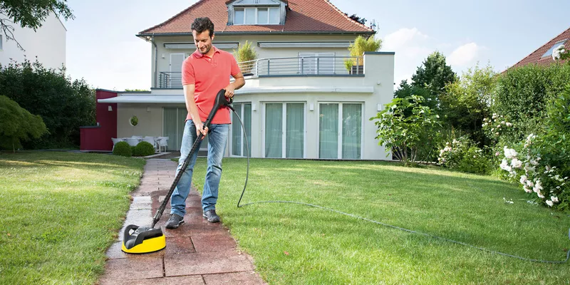 A man cleans the path in front of his house with a combination of a Kärcher pressure washer and an surface cleaner