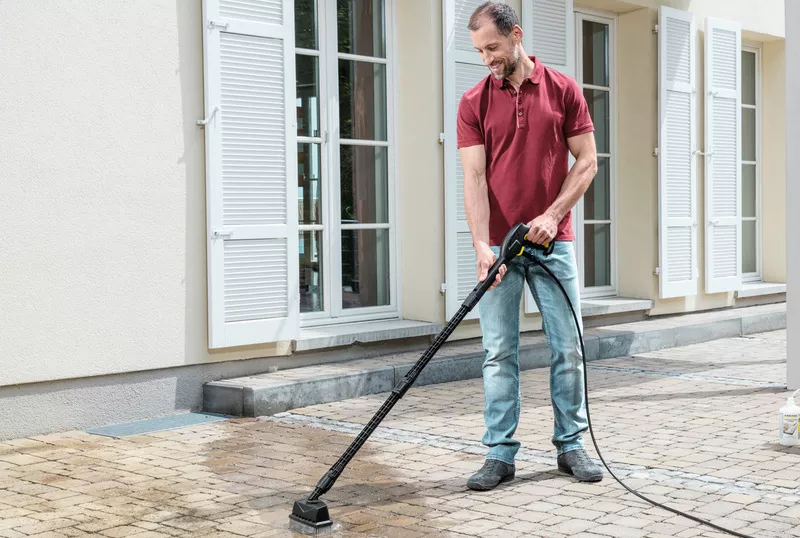 A man cleans paving stones with the Kärcher scrubber attachment
