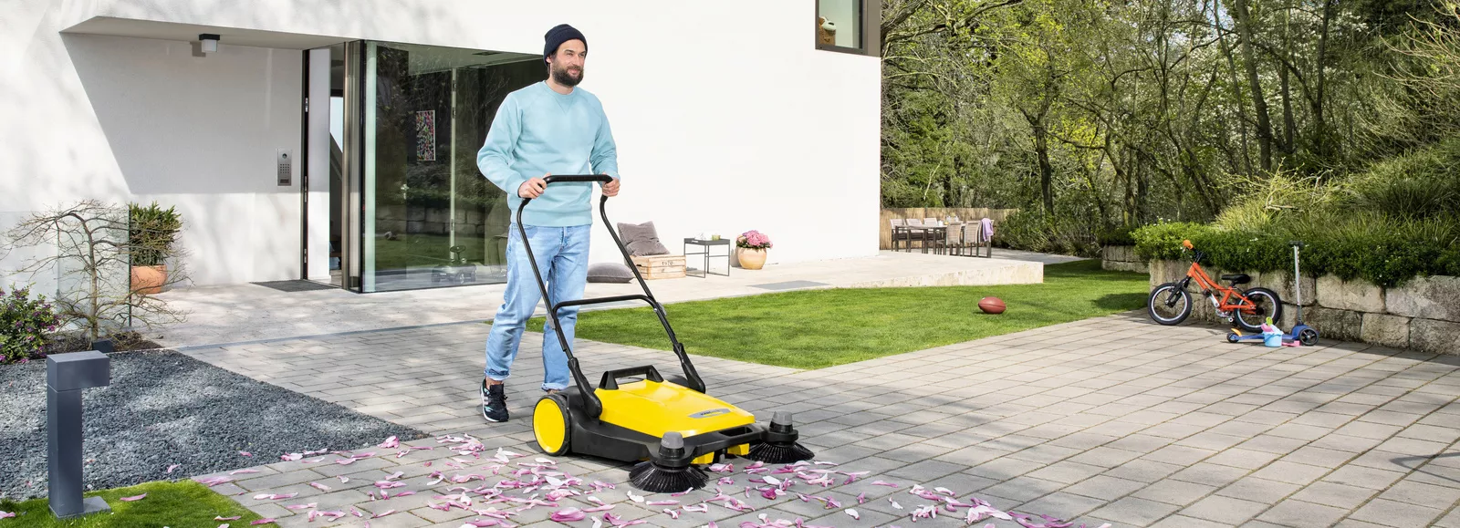 A man cleans paving stones with a Kärcher Sweeper in spring