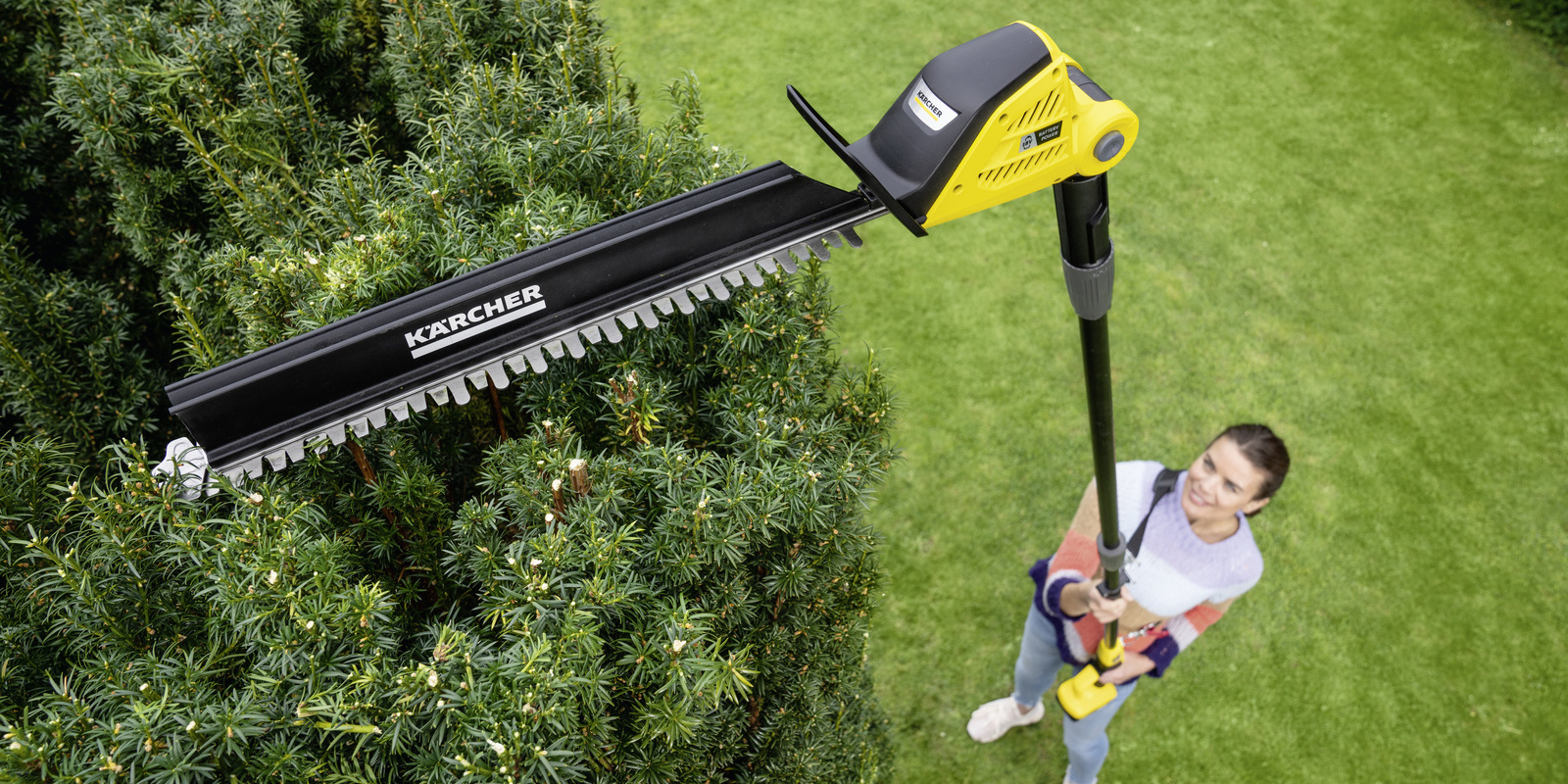 Sägefunktion von oben: Eine Frau schneidet ihre Hecke mit Hilfe der Kärcher Akku-Teleskop-Heckenschere