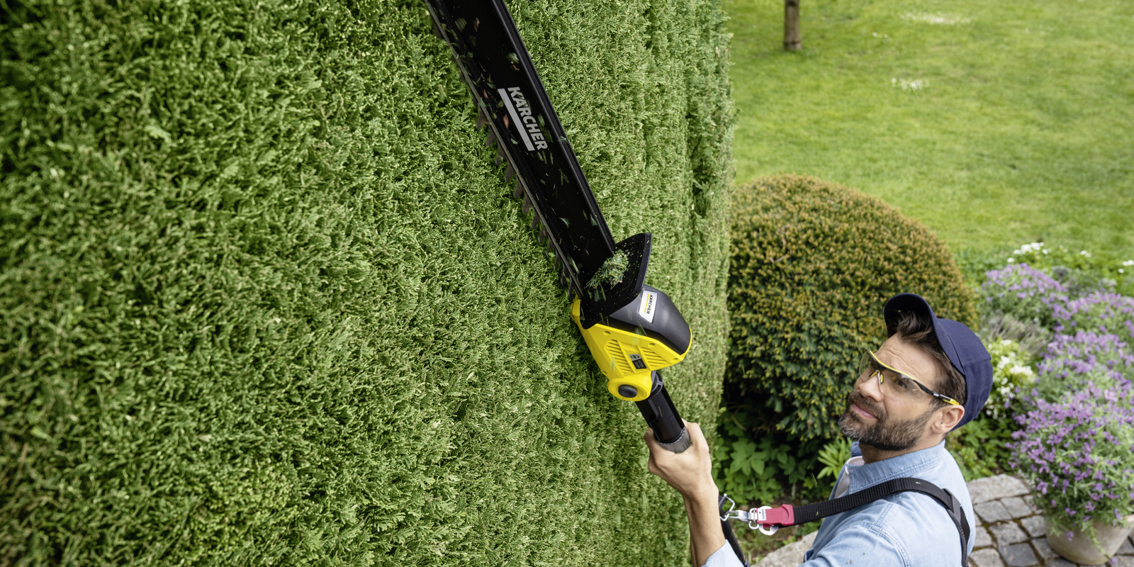 Schultergurt Ein Mann arbeitet mit der Kärcher Akku-Heckenschere über Kopf und nutzt einen Schultergurt