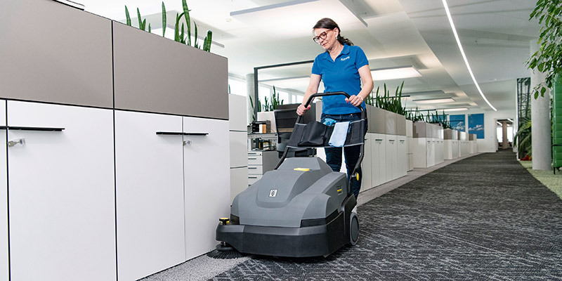 Contract Cleaners A worker vacuums inside an office building with a Kärcher commercial upright vacuum.