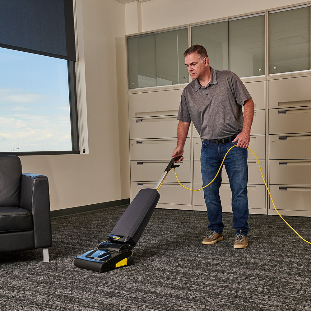 Carpet cleaning in a hotel work center Man uses the Kärcher Ranger upright vacuum in a hotel work center