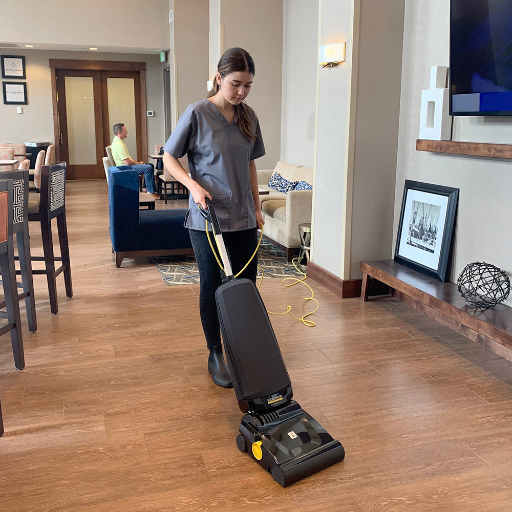 Collecting dust and debris off hard floor surfaces Woman cleans hard floor surfaces in a hotel breakfast area