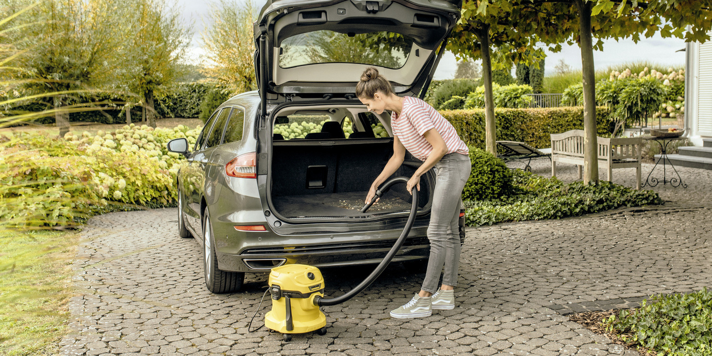 Une femme nettoie le coffre de sa voiture avec un aspirateur Kärcher