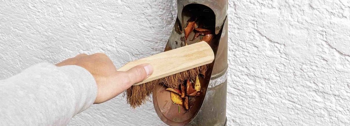Enlever les feuilles mortes du tuyau de descente de la gouttière Les feuilles mortes sont enlevées du tuyau de descente de la maison à l’aide d’un balai