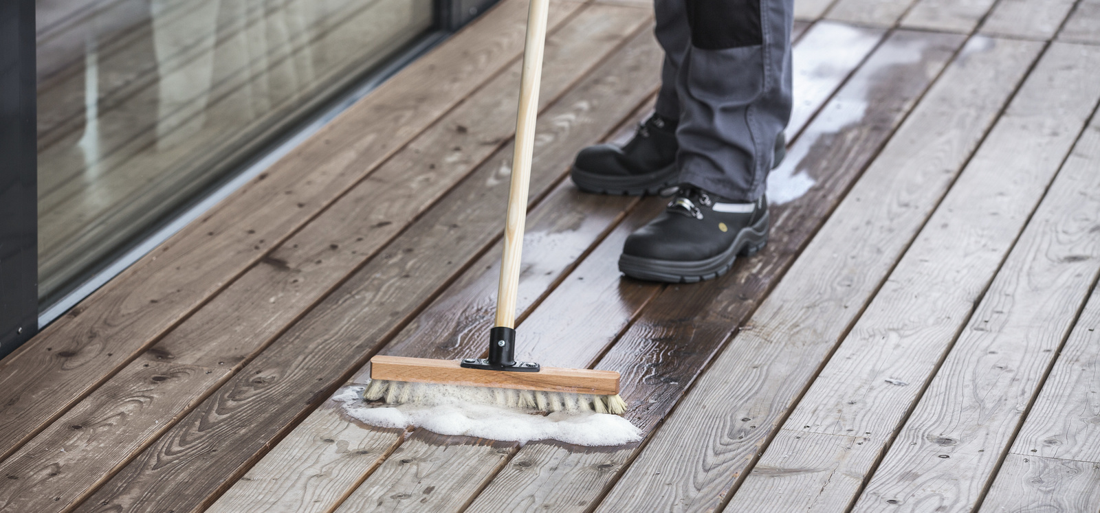 Enlever les dépôts verts Un liquide est répandu sur une terrasse en bois à l’aide d’un balai