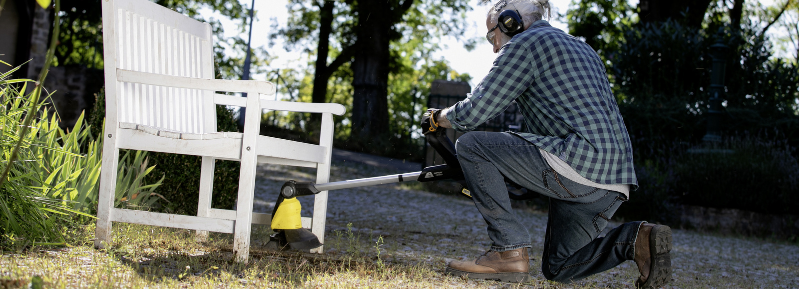 Enlever les mauvaises herbes Un homme enlève les mauvaises herbes sous un banc avec le désherbeur de Kärcher