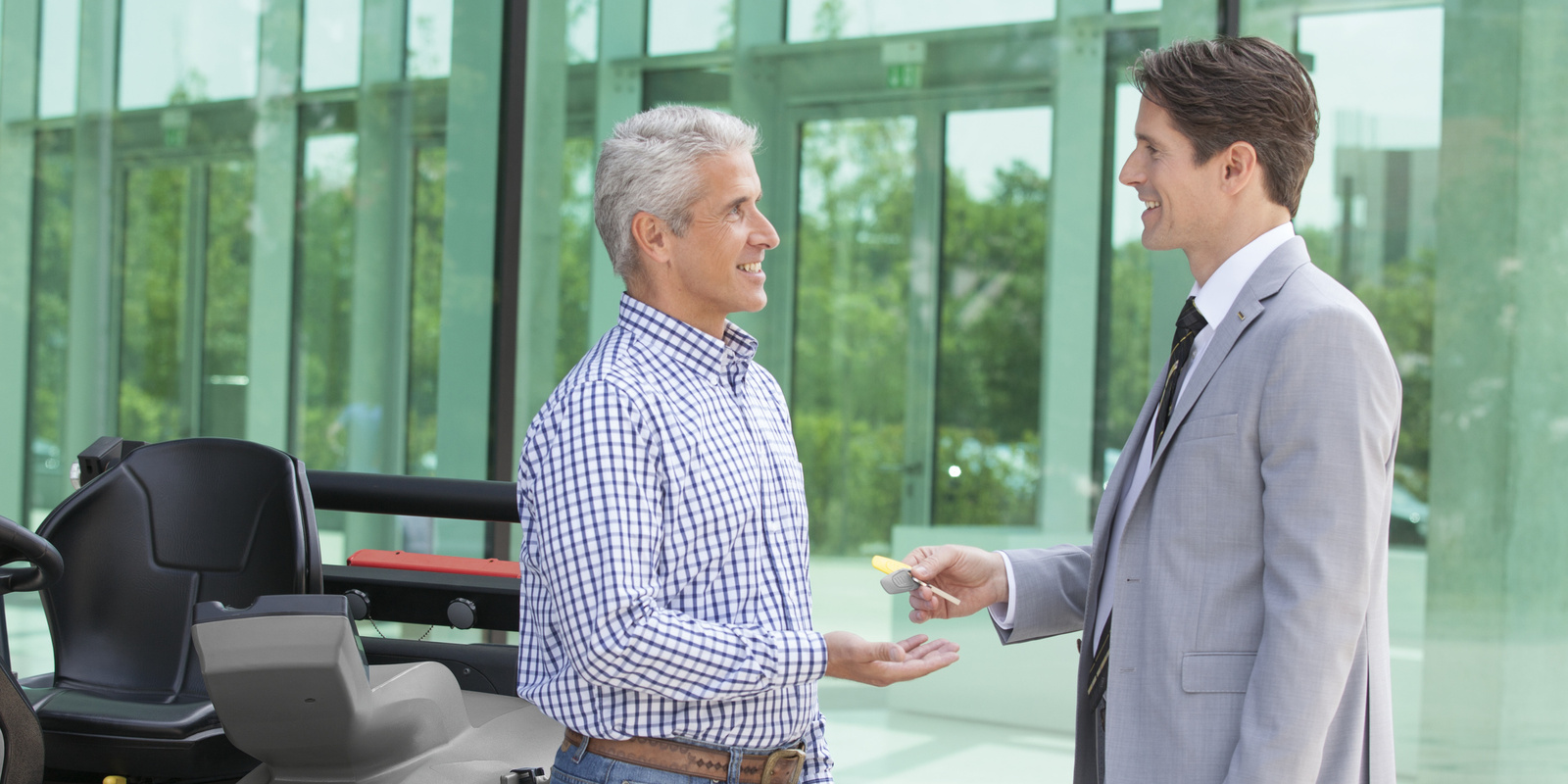 The foundation for good financing is the trust between both contract partners – this is true in the cleaning industry, too. A person in a suit hands another person a key for a Kärcher sweeper machine