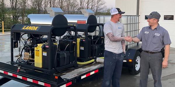Two men shake hands next to a Landa pressure washer