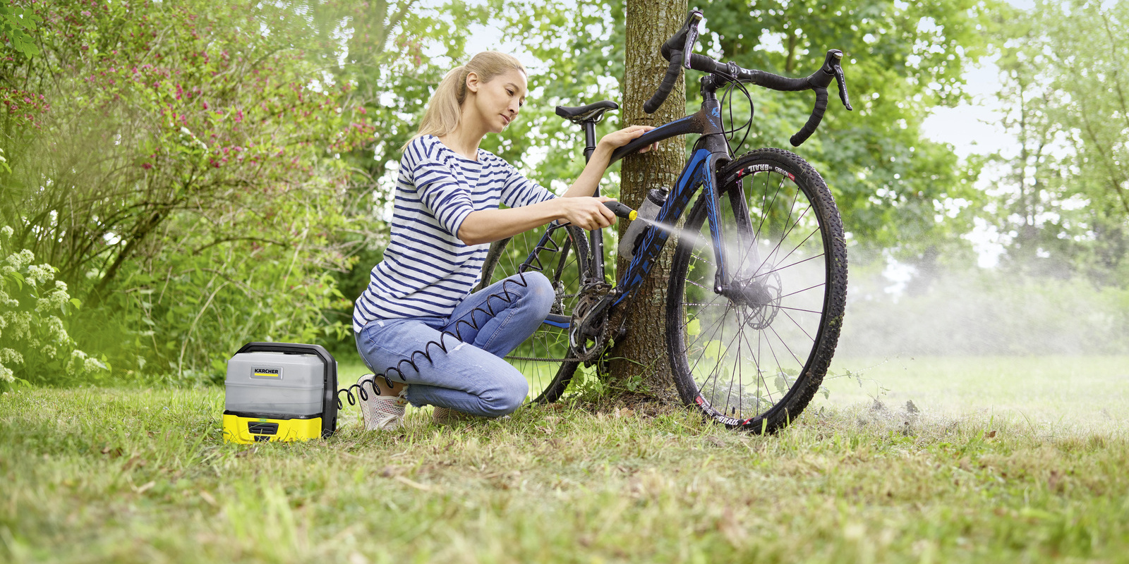 A woman cleans her camping table with a Kärcher: Mobile Outdoor Cleaner