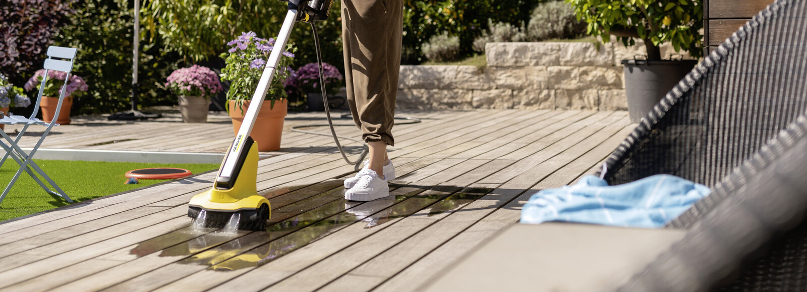 Kobieta za pomocą urządzenia do czyszczenia tarasów Patio Cleaner myje deski tarasowe. Kobieta za pomocą urządzenia do czyszczenia tarasów Patio Cleaner myje deski tarasowe.