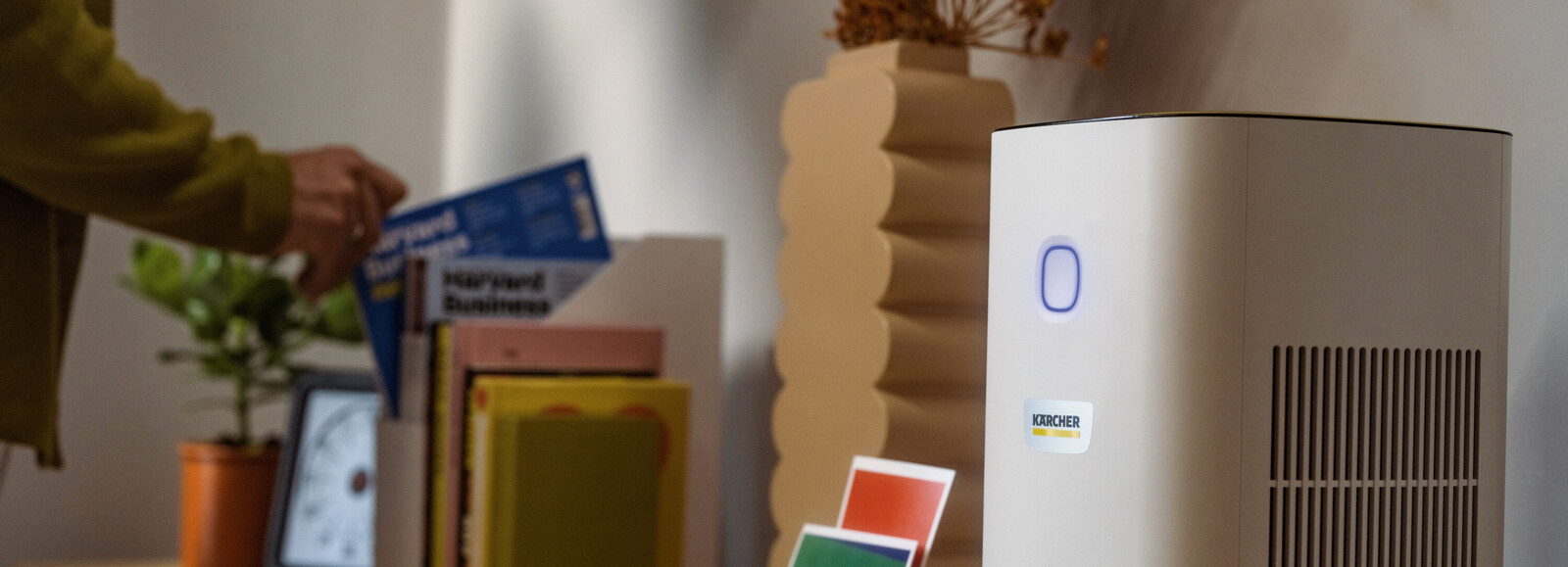 Kompaktowy oczyszczacz powietrza Kärcher AF 20 ustawiony na komodzie obok przedmiotów dekoracyjnych i książek.