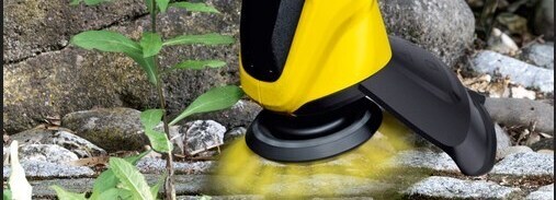 chwasty na kostce brukowej Zbliżenie na obracającą się szczotkę wycinaka do chwastów. Obok rosnące między kostką brukową chwasty.