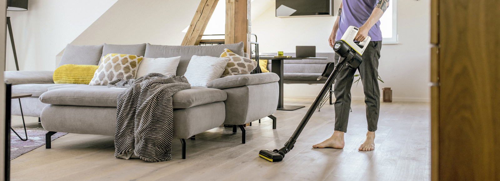 Mężczyzna odkurza podłogę za pomocą odkurzacza pionowego Karcher z serii VC. Mężczyzna odkurza podłogę za pomocą odkurzacza pionowego Karcher z serii VC.