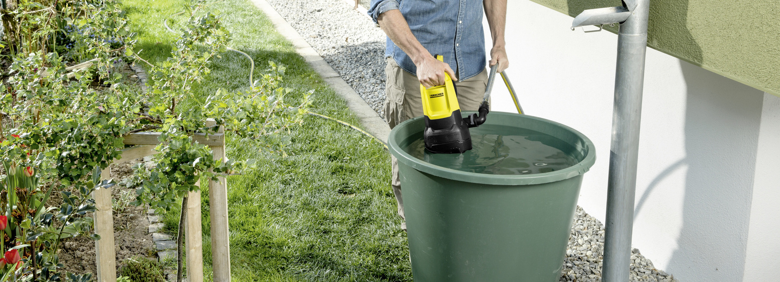 Mężczyzna wkłada do zbiornika na deszczówkę pompę zanurzeniową Karcher. Mężczyzna wkłada do zbiornika na deszczówkę pompę zanurzeniową Karcher.