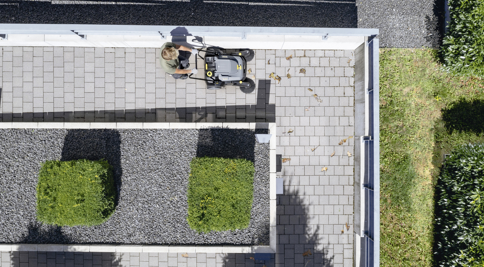 Manual sweeper A person with a manual Kärcher sweeper cleaning a path with cobblestones