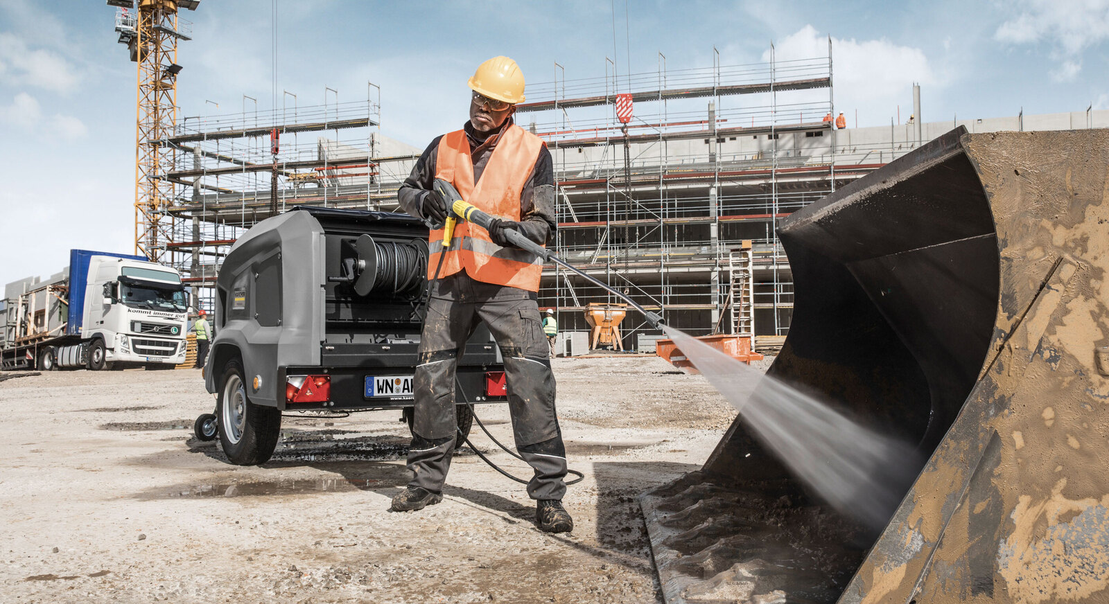 Eine Person mit Hochdruckreiniger säubert eine Baggerschaufel