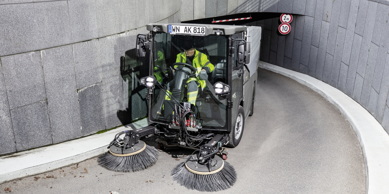 Kehrmaschine von Kärcher eine Person sitzt im Führerhäuschen einer Kehrmaschine und fährt aus einem Parkhaus