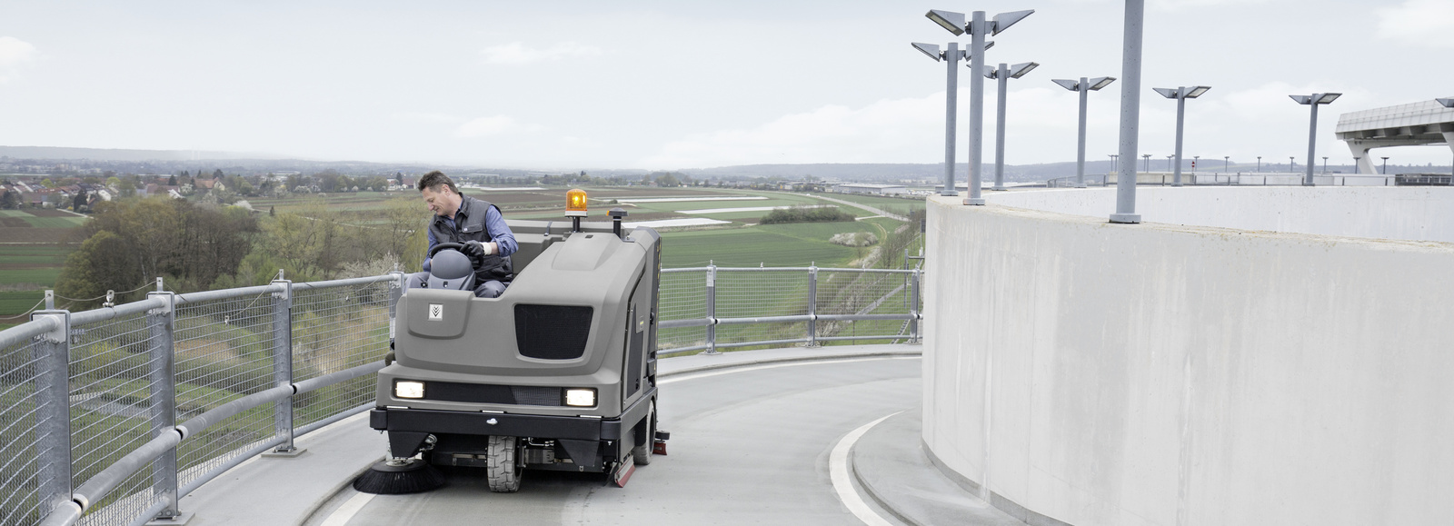 Ride-on sweeper in use A person driving up the road of a parking deck with a Kärcher sweeper