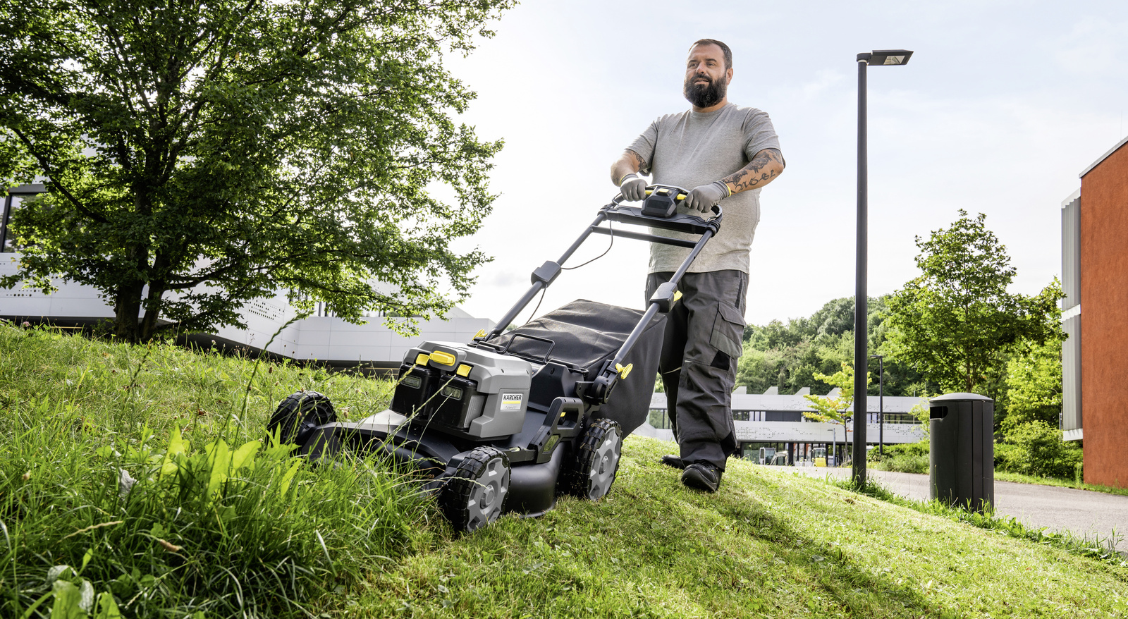 Lawn mower in use A person trimming a green area on a slope with a Kärcher lawn mower