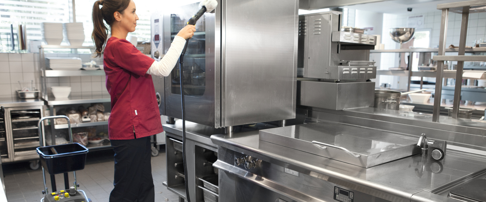 Oberflächenreinigung in der Großküche Eine Person säubert mit einem Dampfreiniger einen Küchenschrank