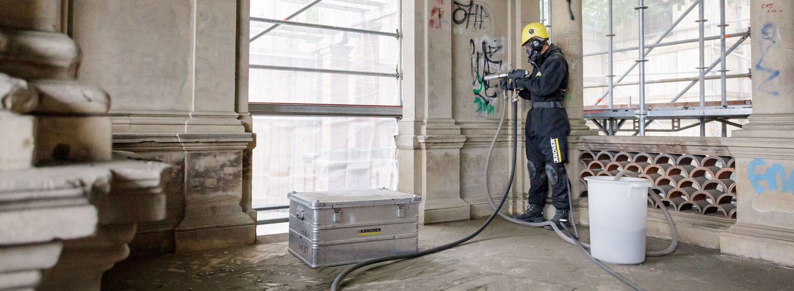 Graffiti entfernen Eine Person entfernt mit einem Hochdruckreiniger Graffiti von einer Wand