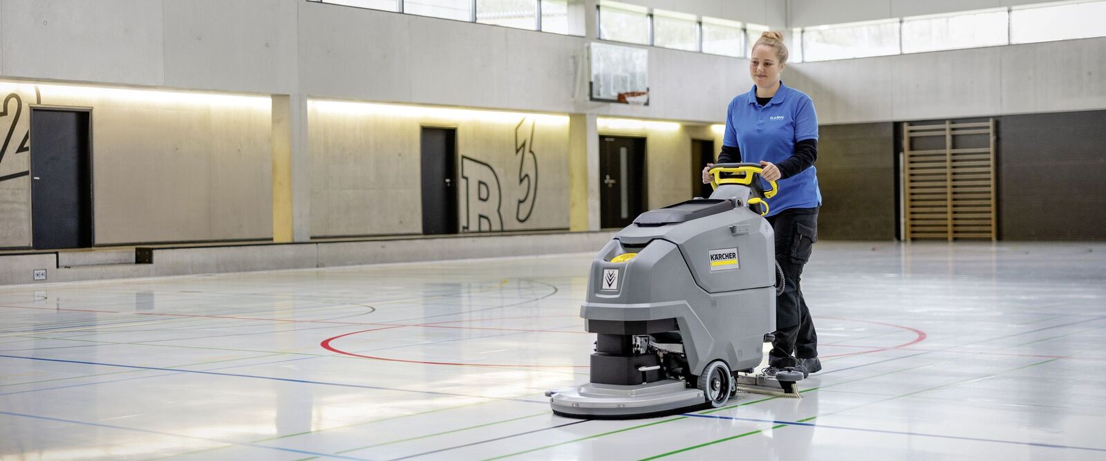 Turnhalle reinigen Eine Person reinigt mit einer Scheuersaugmaschine eine Turnhalle