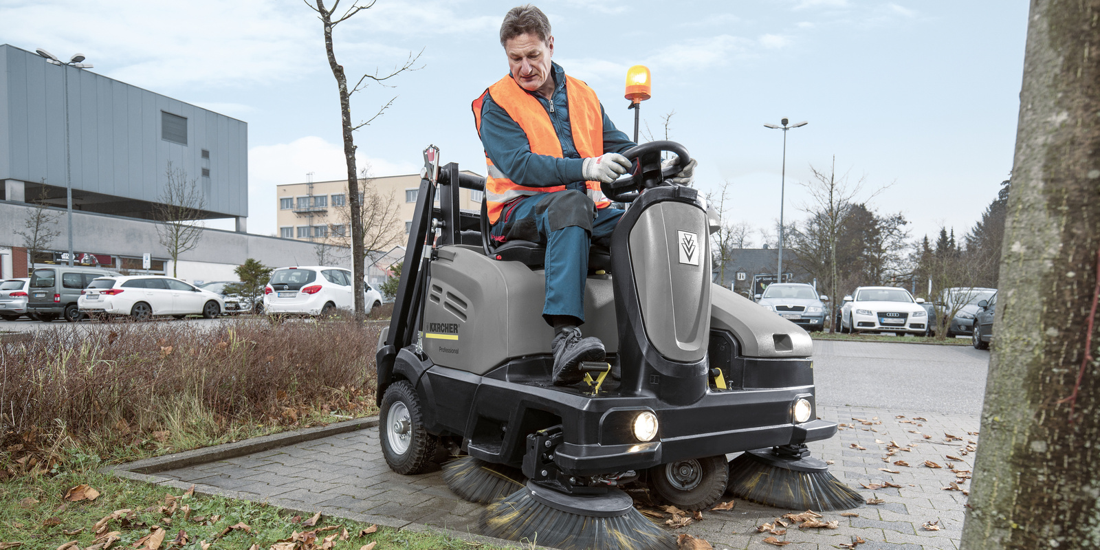 Ride-on vacuum sweeper in use A person sitting on a Kärcher ride-on vacuum sweeper cleaning a parking lot