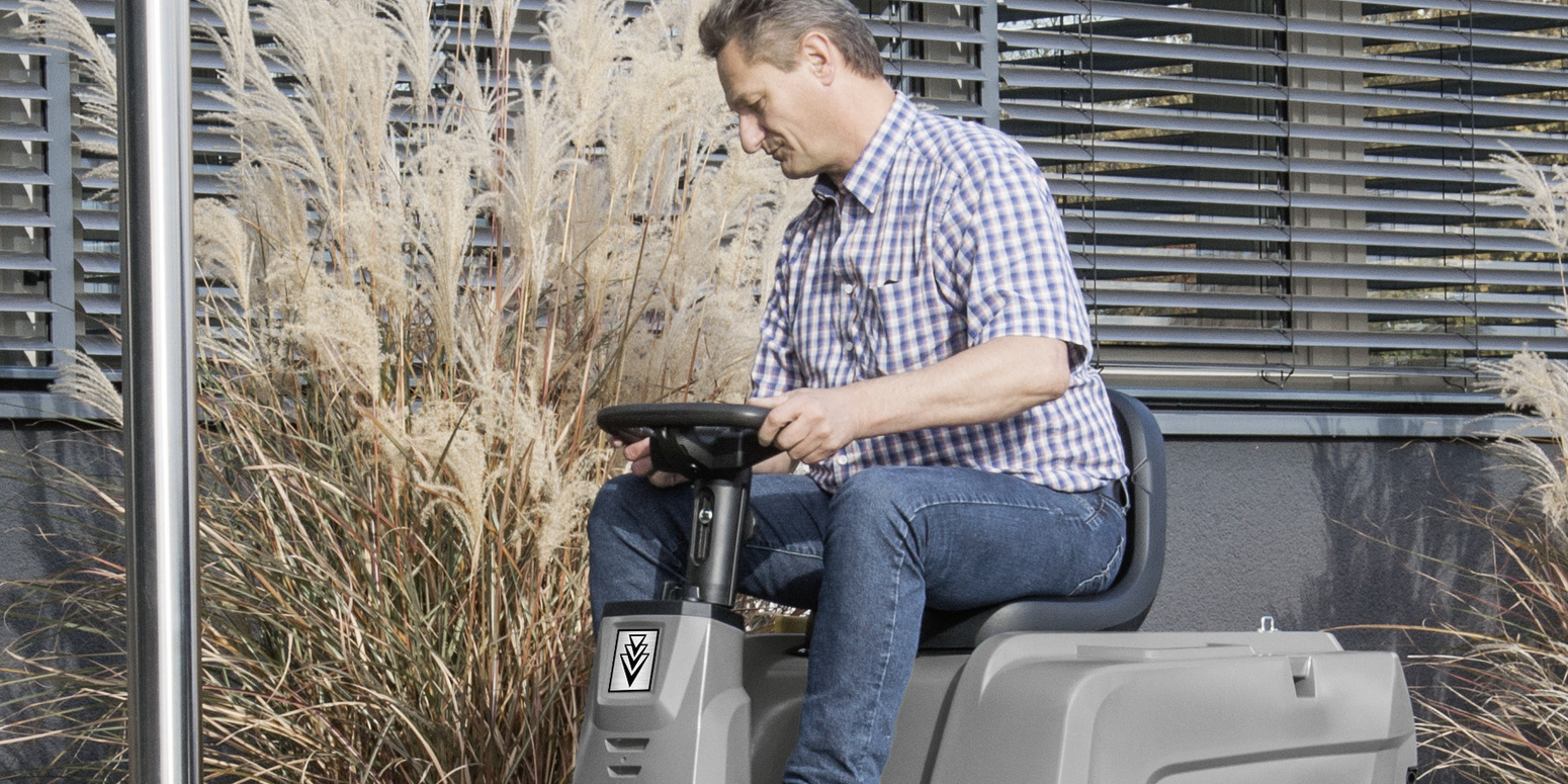 Ride-on vacuum sweeper in use A person sitting on a Kärcher ride-on vacuum sweeper