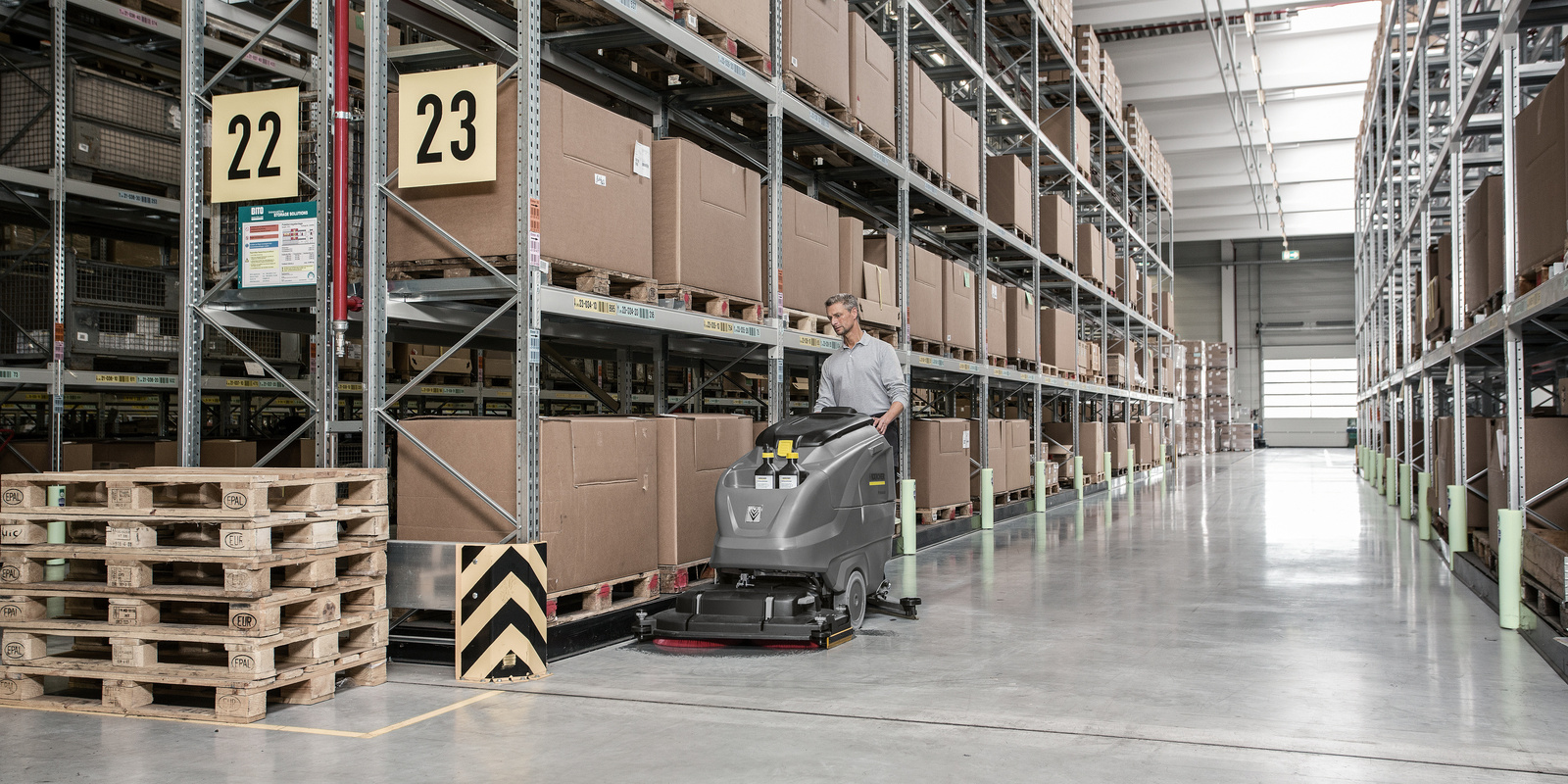 Cleaning in logistics A person cleans a warehouse with a Kärcher sweeper