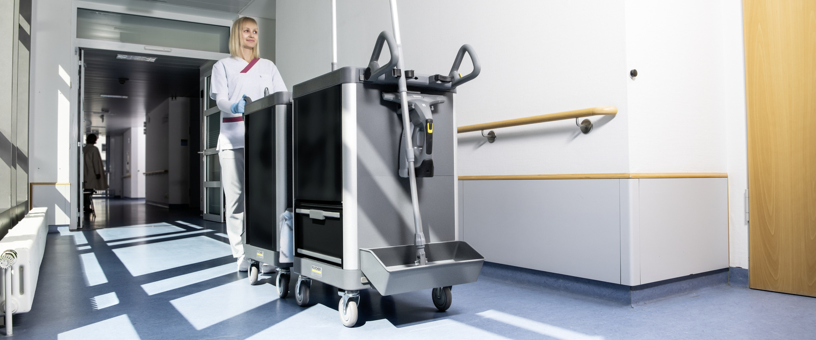 Reinigungswagen von Kärcher Eine Person läuft mit einem Reinigungswagen von Kärcher einen Gang entlang