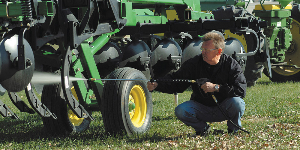 A farmer pressure washes ag equipment using a Hotsy pressure washer