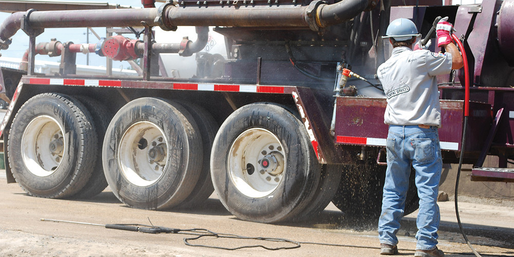 A worker washes heavy equipment with a Hotsy pressure washer