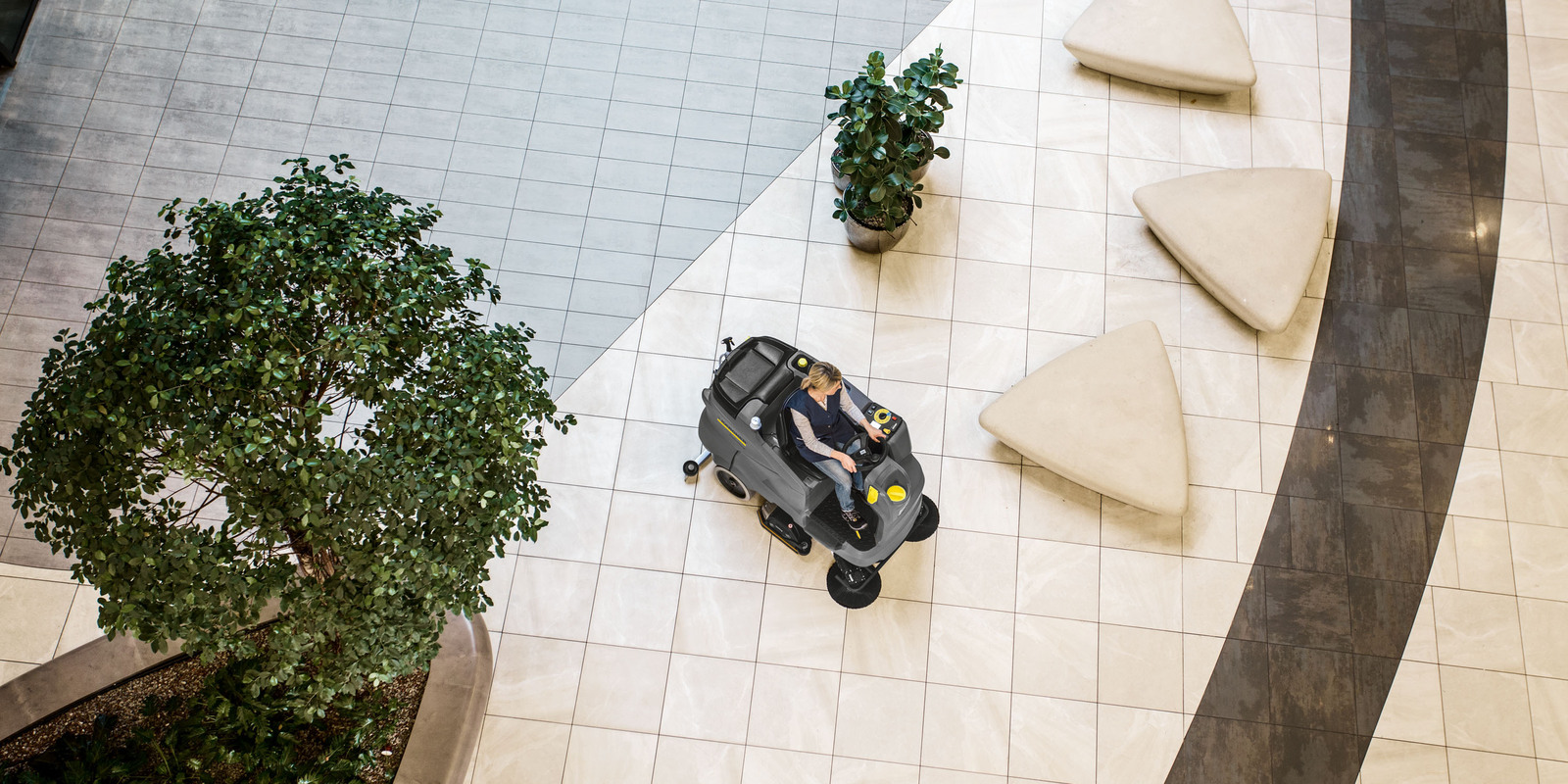 The ride-on scrubber dryer in use A person cleaning the extensive floor with a Kärcher ride-on scrubber dryer