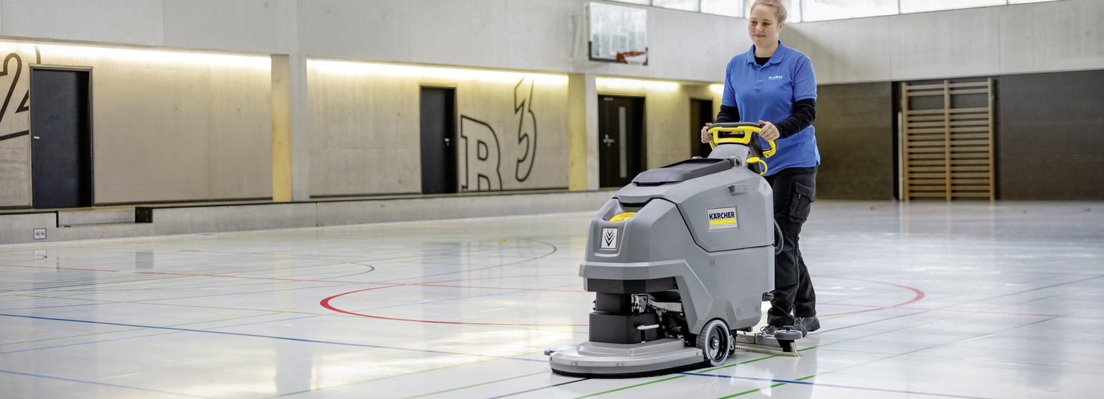 Scrubber dryer in use A woman cleaning the floor of a gym with a large scrubber dryer