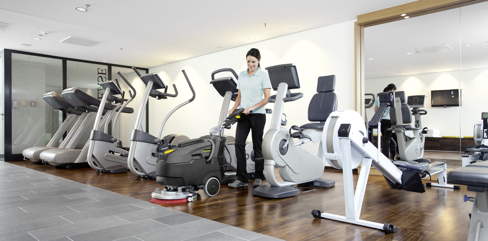 Cleaning with the scrubber dryer A woman cleans a fitness area with a Kärcher scrubber-dryer
