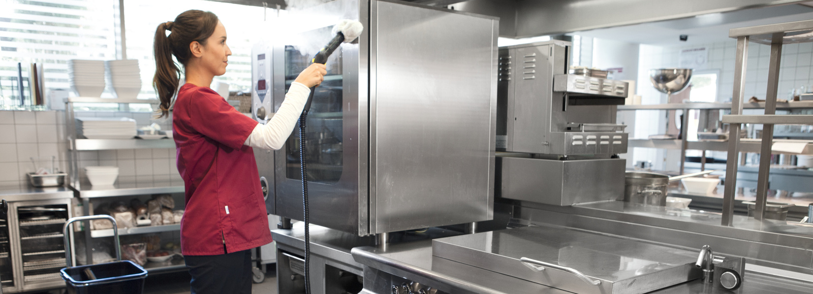 Steam cleaner in use A woman is cleaning the surface of a kitchen cabinet with a steam cleaner