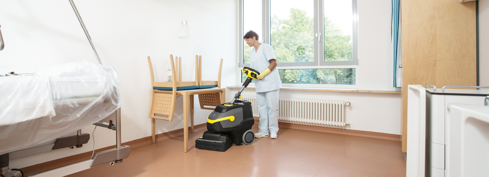 Scrubber dryer in use A woman cleaning the floor of a patient room with a scrubber dryer