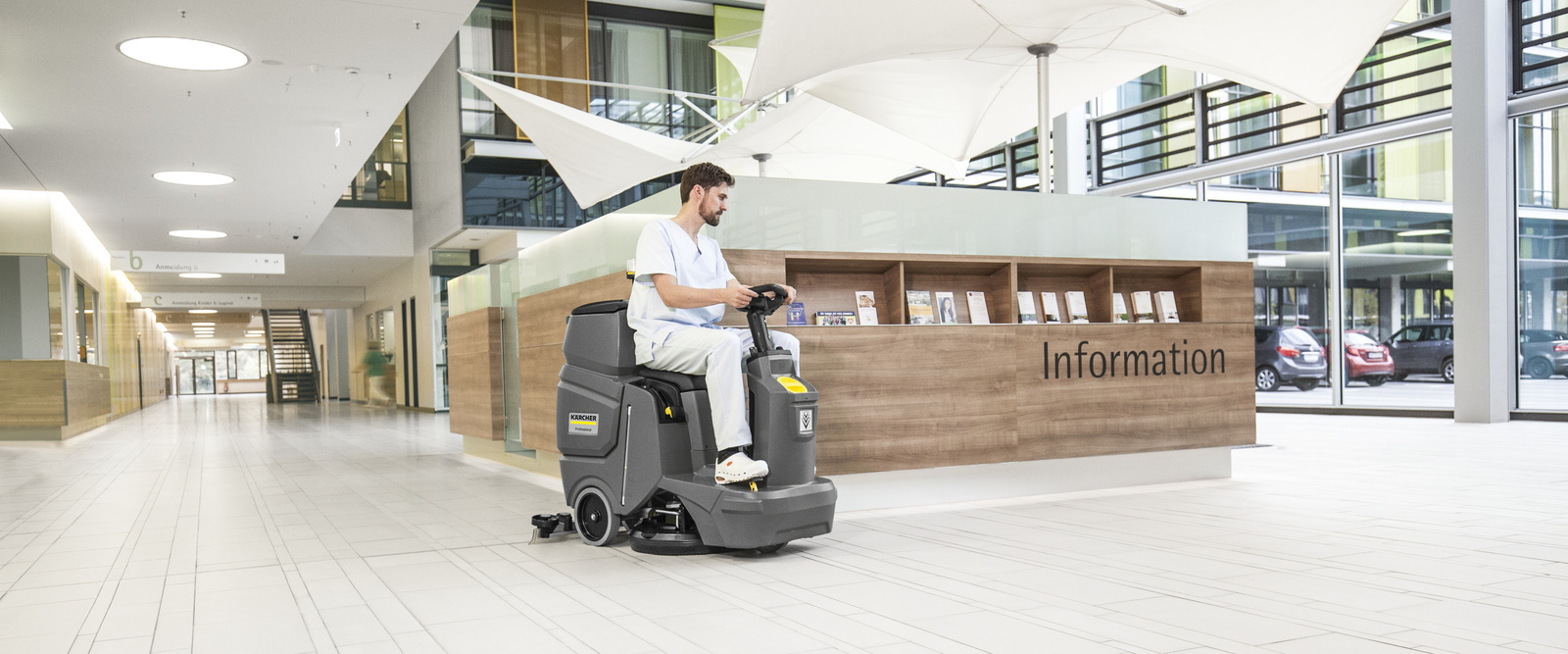 Ride-on vacuum sweeper in use A person cleaning the floor in the reception area with a Kärcher ride-on vacuum sweeper