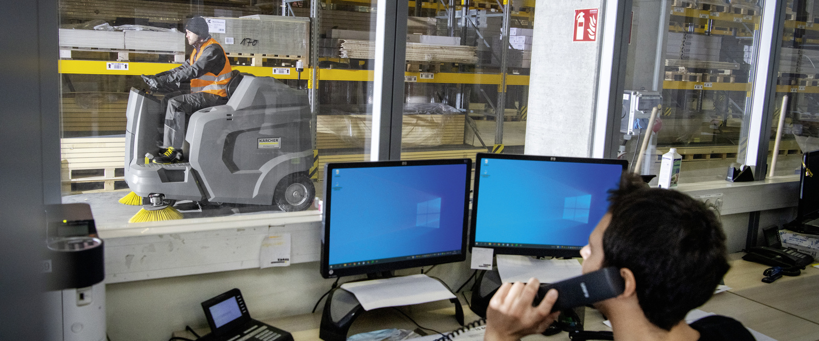 Ride-on vacuum sweeper in use A person cleans the floor in the warehouse with a ride-on vacuum sweeper