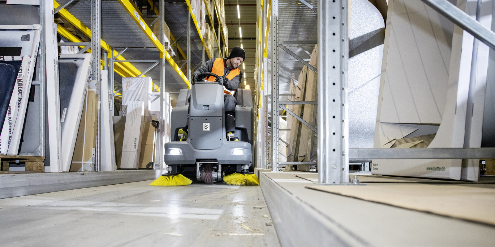Cleaning in the warehouse with a ride-on vacuum sweeper A person cleaning the interior of a warehouse with a ride-on vacuum sweeper