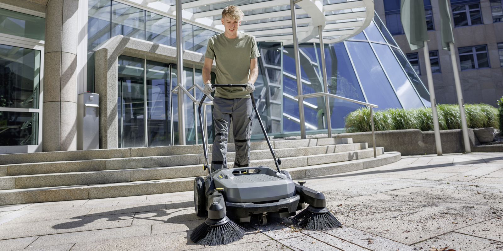 Cleaning with the walk-behind sweeper A person cleaning the outdoor area with the walk-behind sweeper